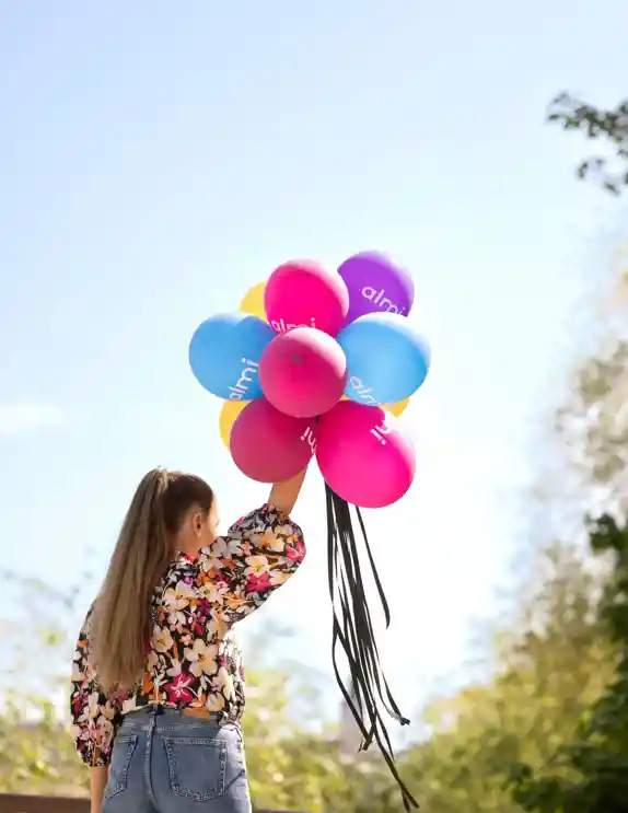 kvinna i blommig blus och jeans håller  i ett gäng ballonger upp i luften och solen skiner